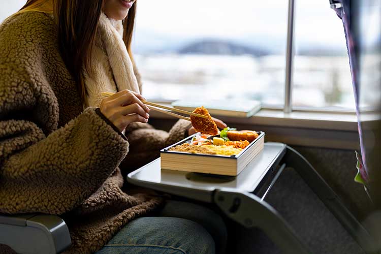 新幹線で駅弁を食べる女性