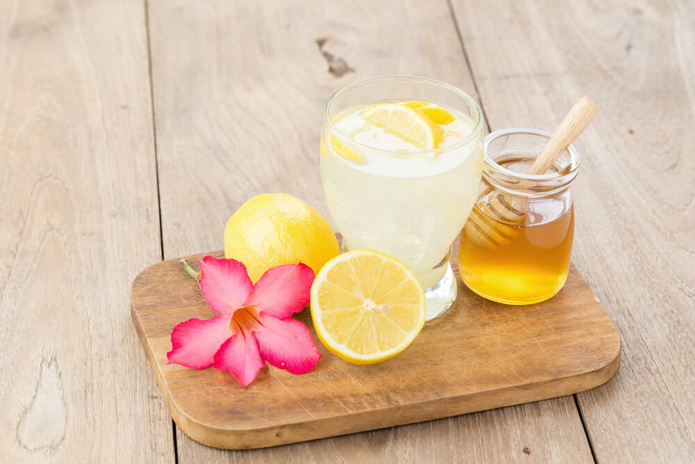 木製テーブルの上の板に乗せられた蜂蜜とレモンと炭酸ドリンク