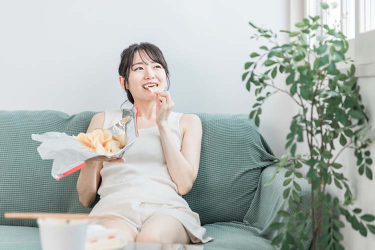 小腹が空いてポテトチップスを食べる女性